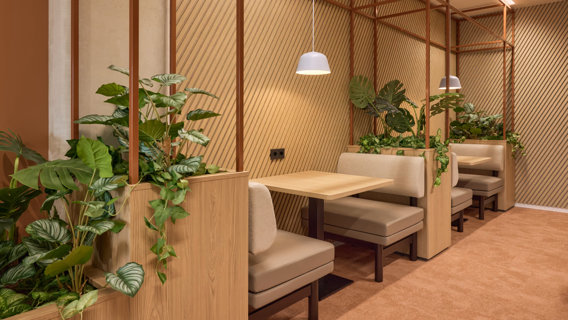 Interieur van een moderne eetruimte met houten scheidingswanden, beige beklede banken en tafels, verlicht door witte hanglampen, met groene planten bij elke eetplek.