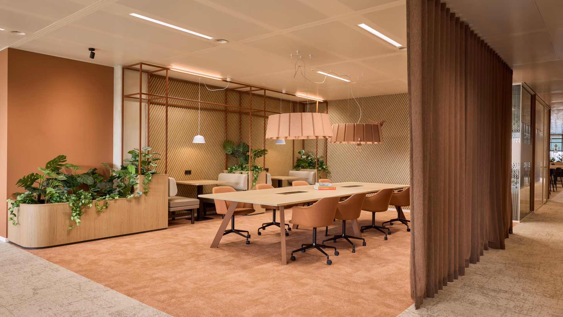 Moderne vergaderruimte met lange tafel, zes draaibare stoelen in bruintinten, grote plantenbak, hanglampen en decoratieve houten wandpanelen.