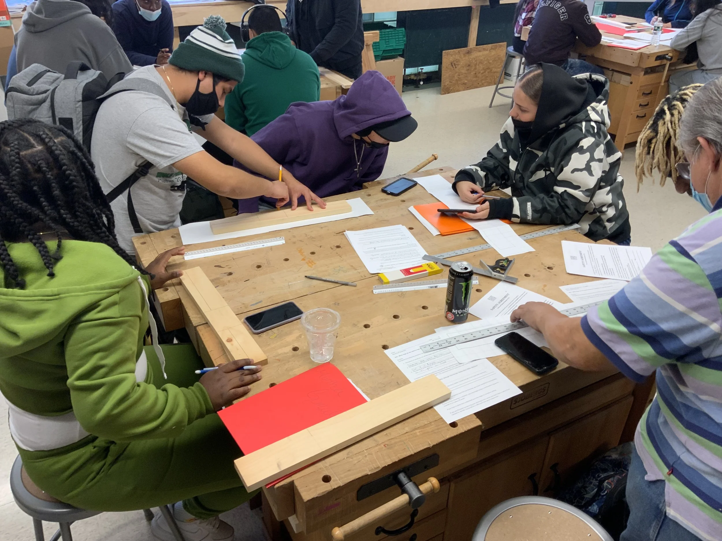 Students measuring and drafting plans at a woodshop workbench