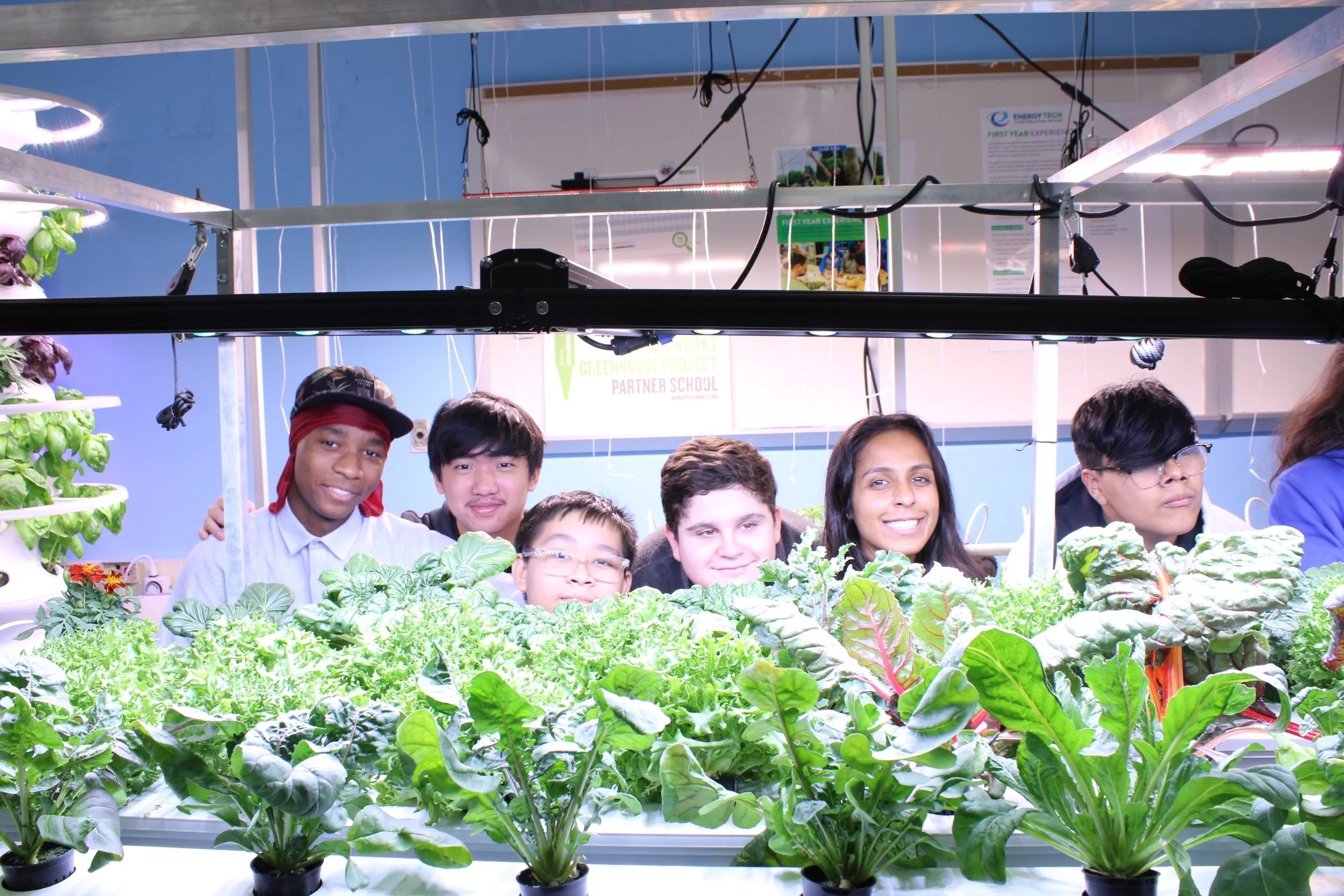 Students and teacher pose behind hydroponic garden growing leafy vegetables indoors