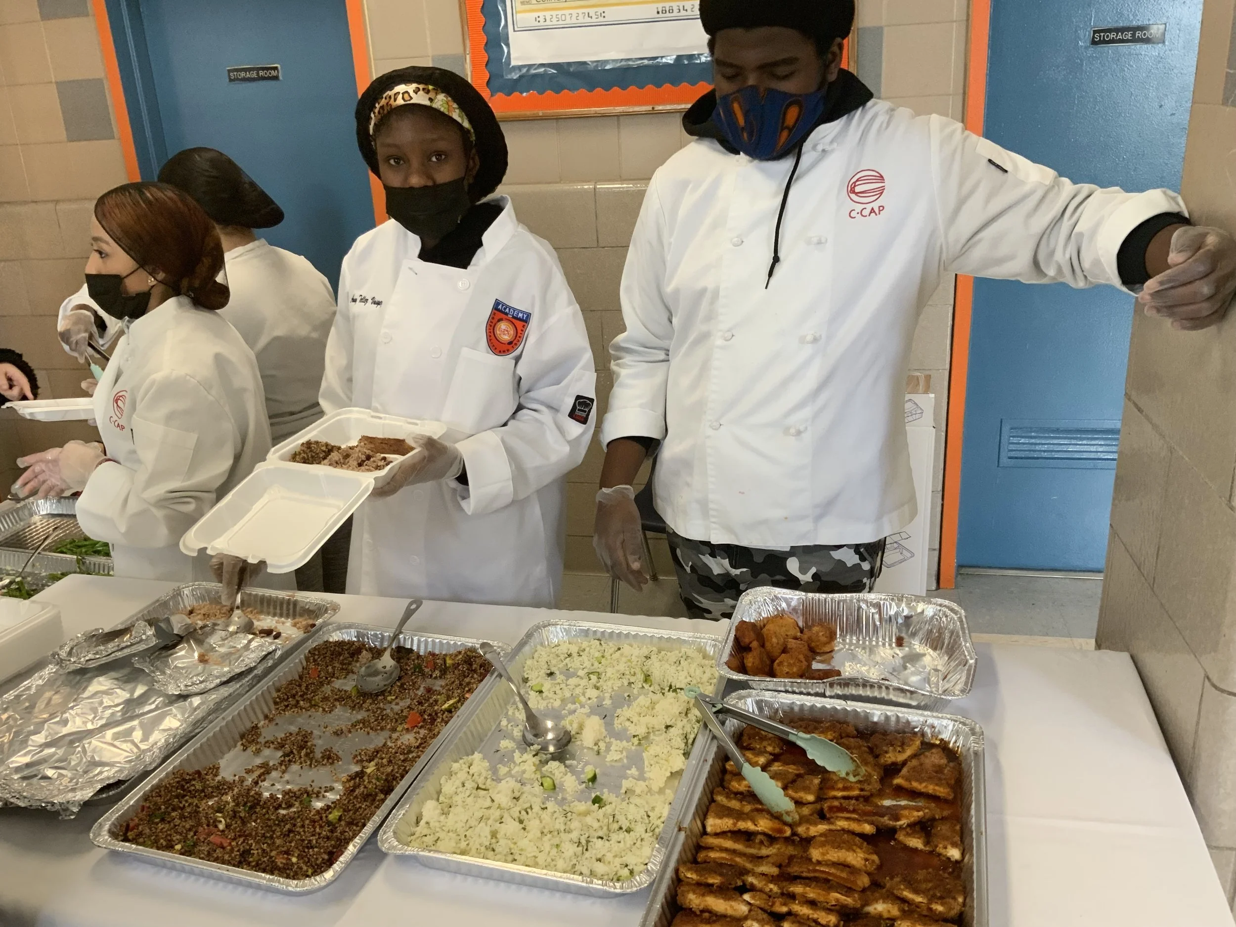 Students in chef coats serving food at a school culinary event