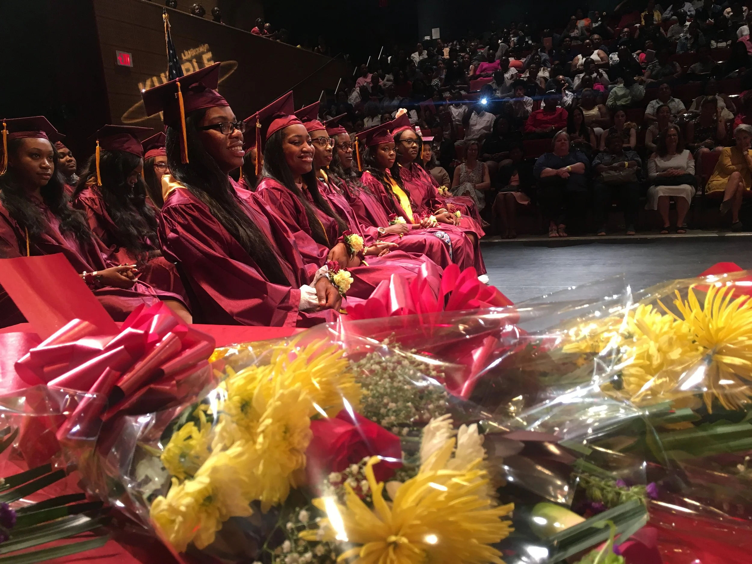 Students in maroon cap and gown seated at graduation ceremony with flowers