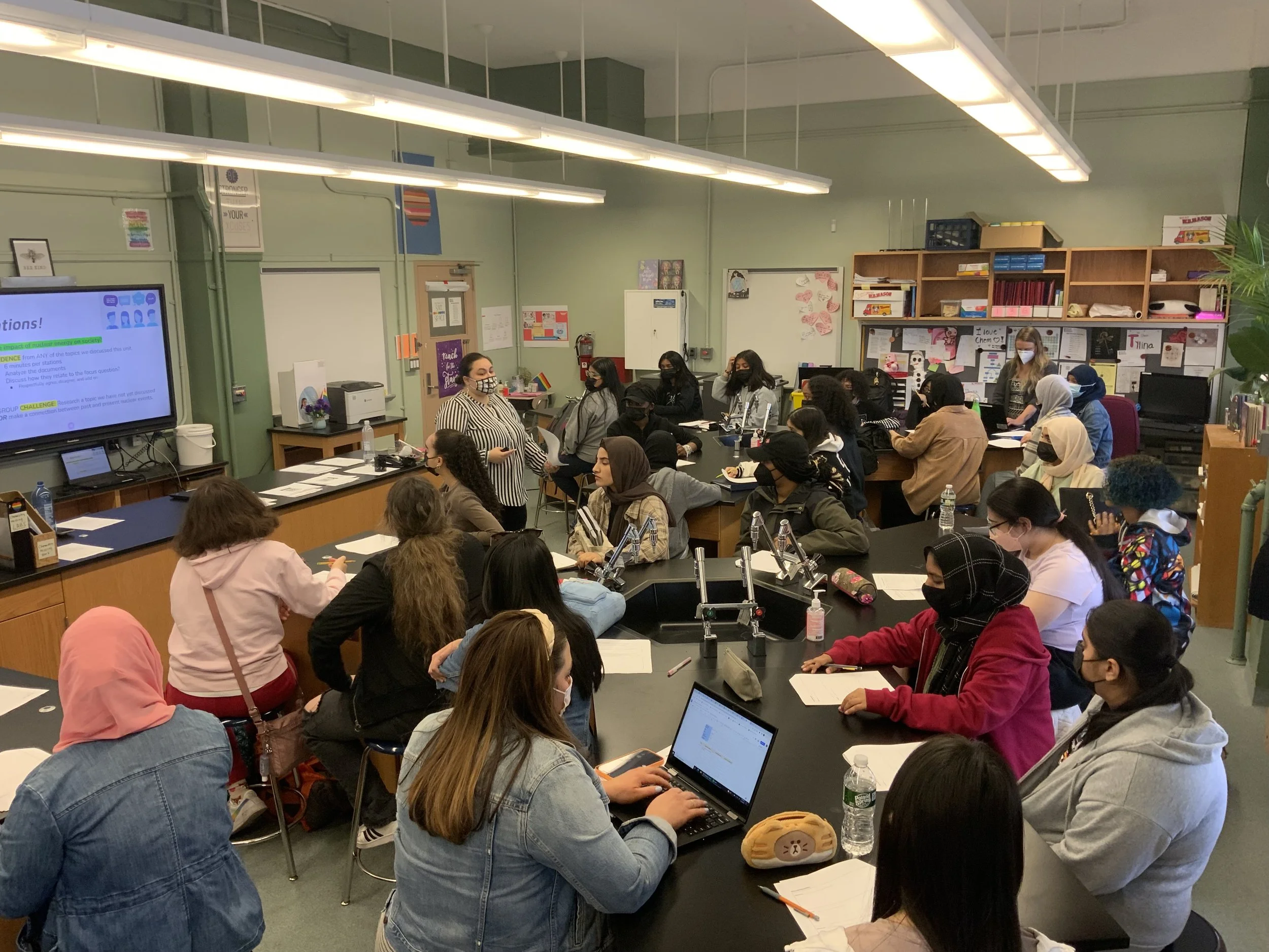 Students attend a science class lesson with teacher presenting at screen