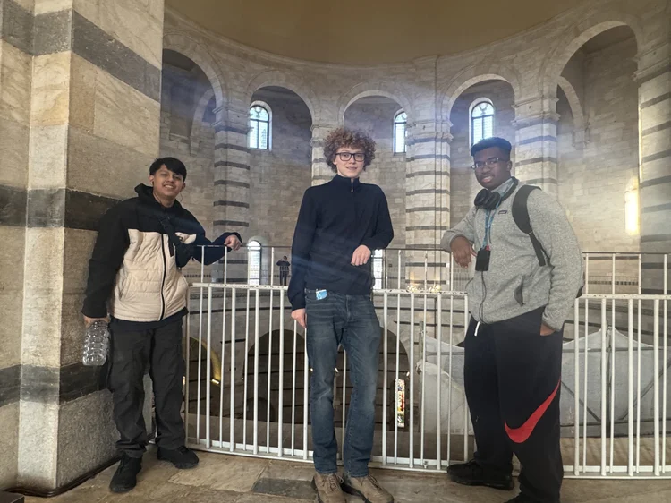 Three students posing inside a historic stone building with arched walls