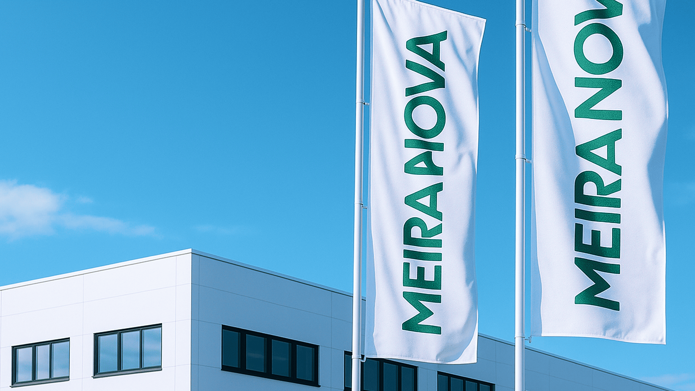 Ulkokuva Meira Novan logistiikkakeskuksesta. Rakennuksen edessä liehuvat Meira Nova -tekstillä olevat liput.