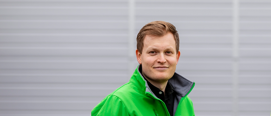 Mies vihreässä takissa harmaata taustaa vasten.
