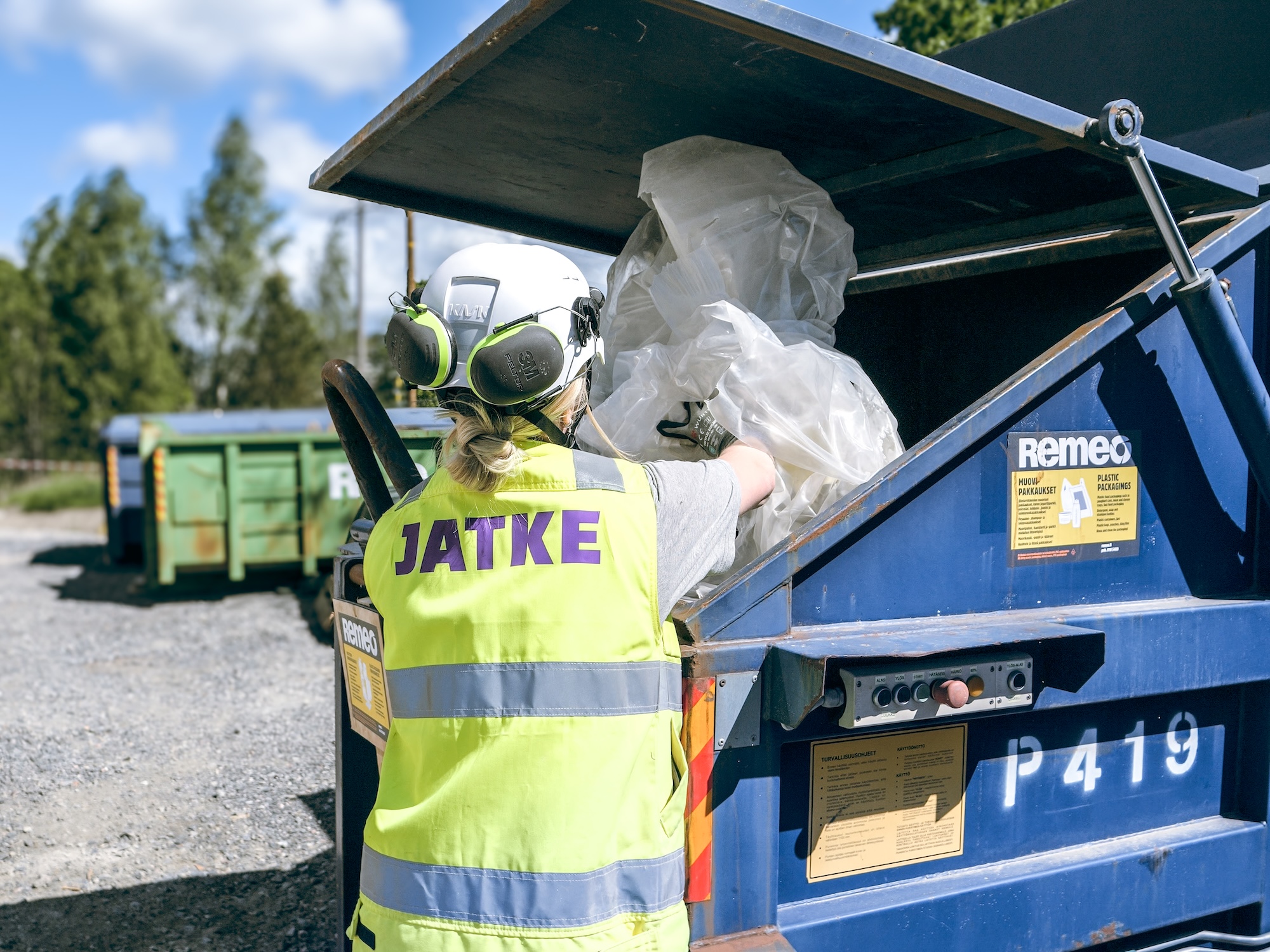 Jatkeen työntekijä laittamassa muovijätettä keräysastiaan.
