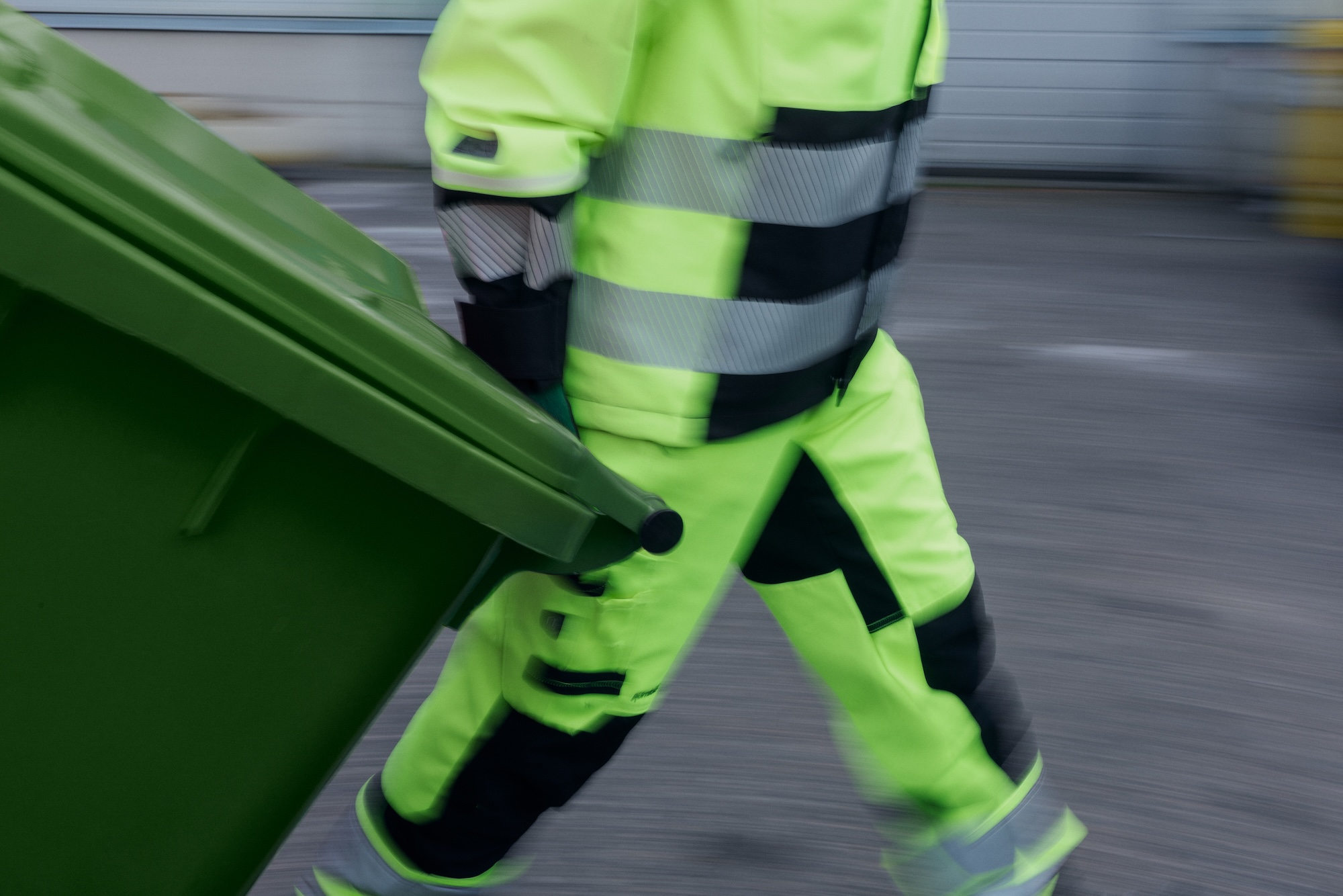 Huomiovaatteisiin pukeutunut työntekijä siirtää jäteastiaa.