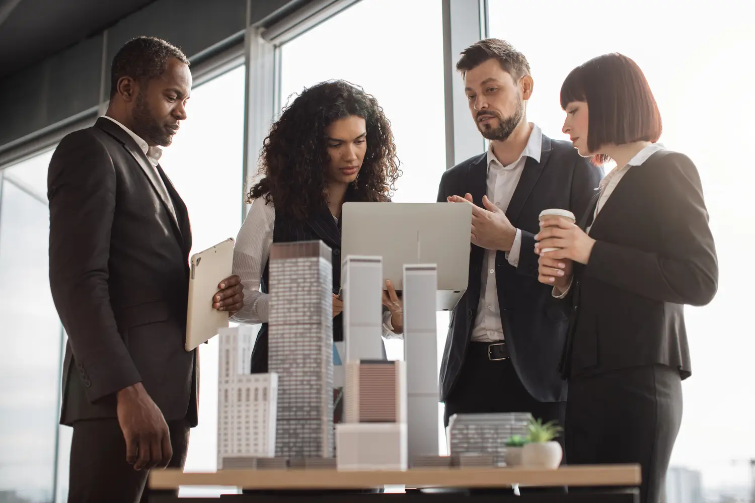 Four people are in a modern, urban workspace. Two women and two men are viewing an architectural model of city buildings.