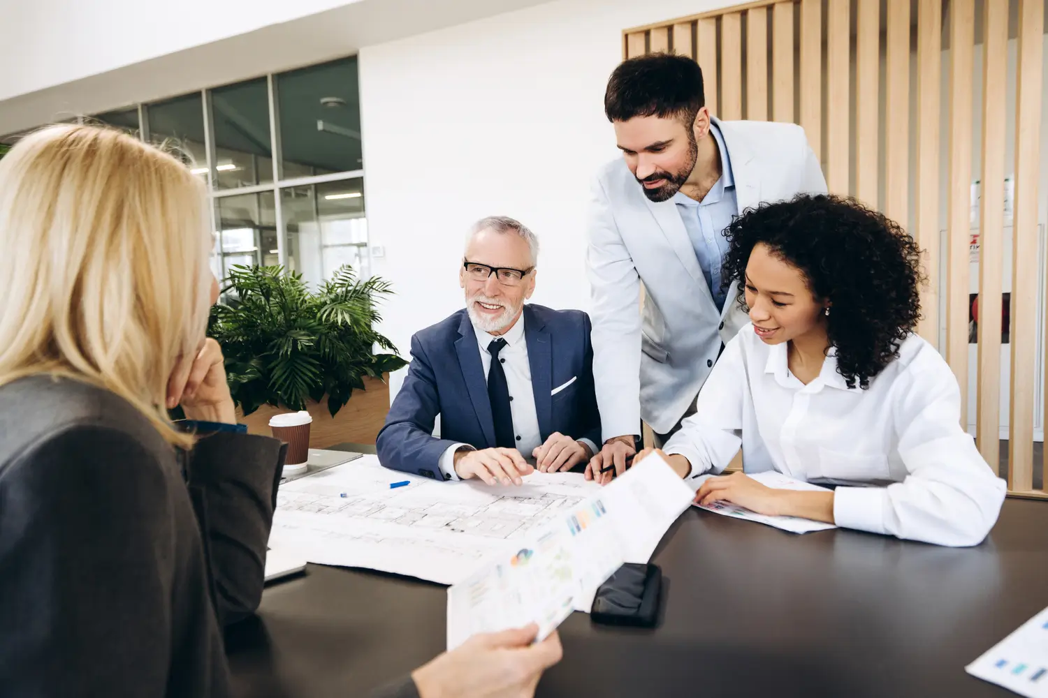 Four individuals are gathered around a dark table in what appears to be a bright, modern office space.
