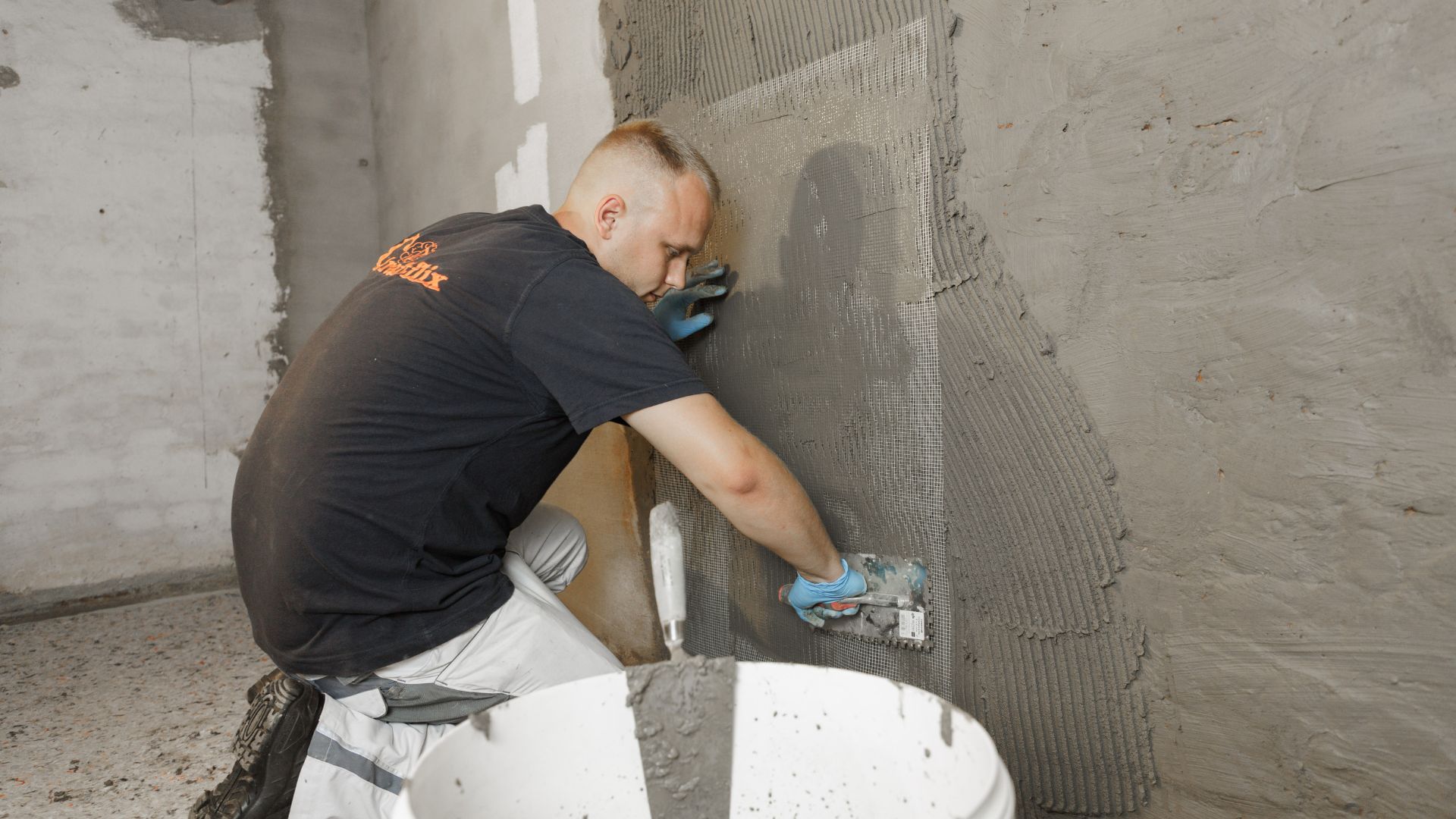 Handwerker trägt Putz auf Kellerwand auf.