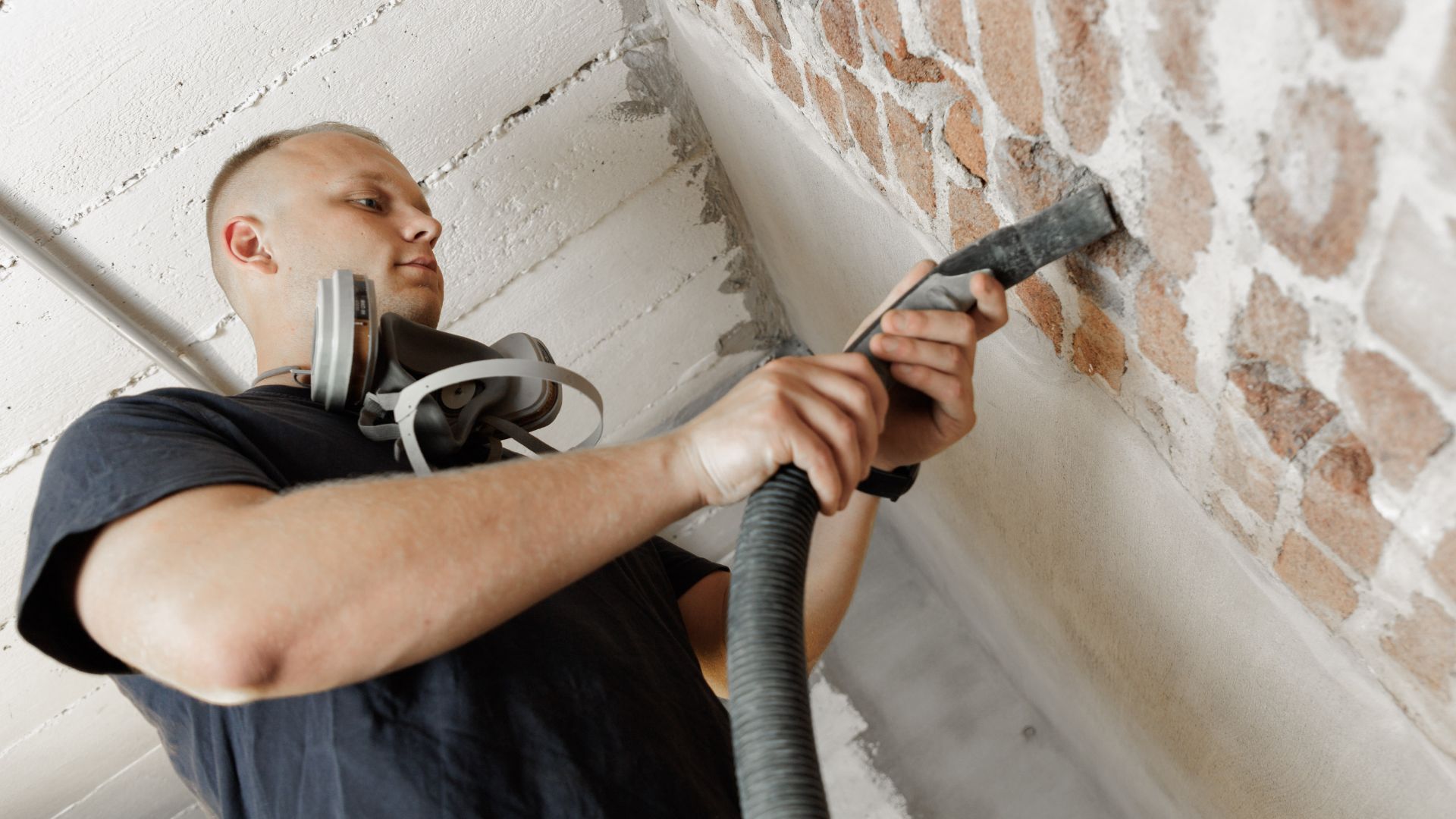 Handwerker saugt Staub aus einer Bohrung in einer Kellerwand