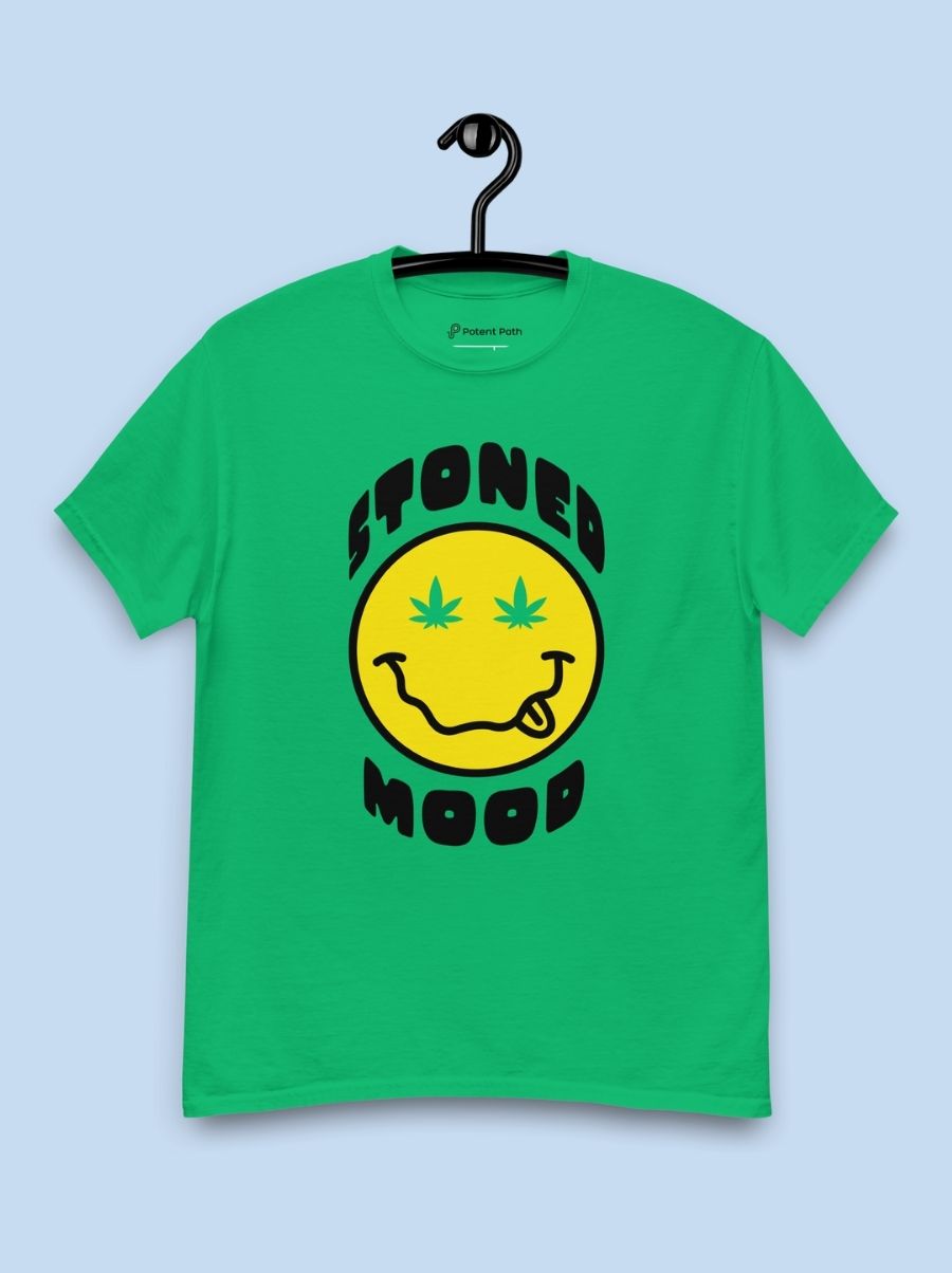 Green t shirt on a hanger and light blue background with a yellow smiley face graphic on the front surrounded by the words 'Stoned Mood'
