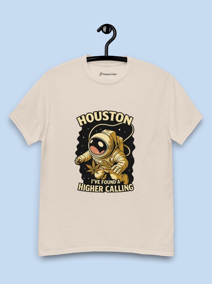 A beige T-shirt on a hanger in front of a blue background with a design on the shirt's chest of an illustrated astronaut holding a leaf and the text "Houston, I've Found a Higher Calling"