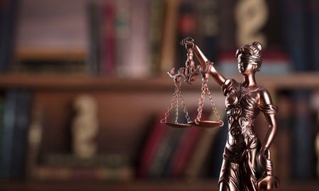 A focused statue of lady justice with a faded book case behind her