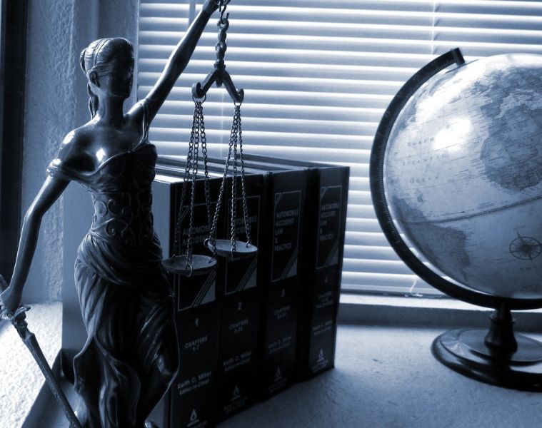 Lady Justice statue next to law books and a globe on a table, in a blue-toned colour scheme