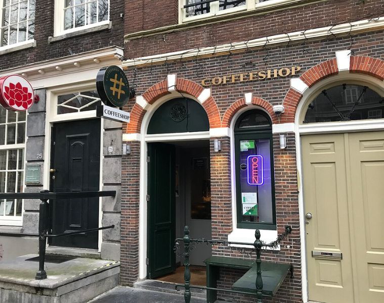 Exterior of a cannabis coffeeshop in Amsterdam made of bricks with an arched doorway, and a neon 'open' sign