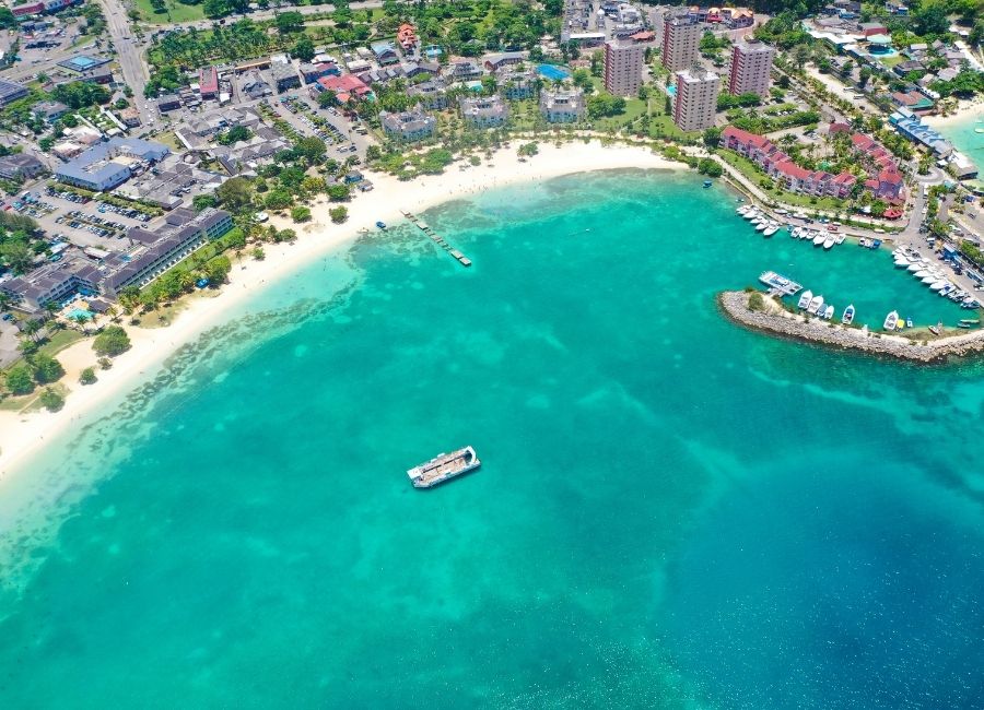 Aerial view of Ocho Rios Bay Beach in Jamaica, showing turquoise water, white sand, and resorts along the coastline