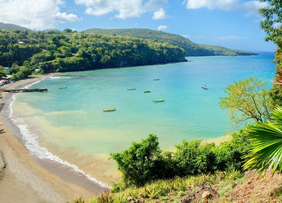 Peaceful bay in Saint Lucia with small boats anchored near golden sand and surrounded by tropical greenery