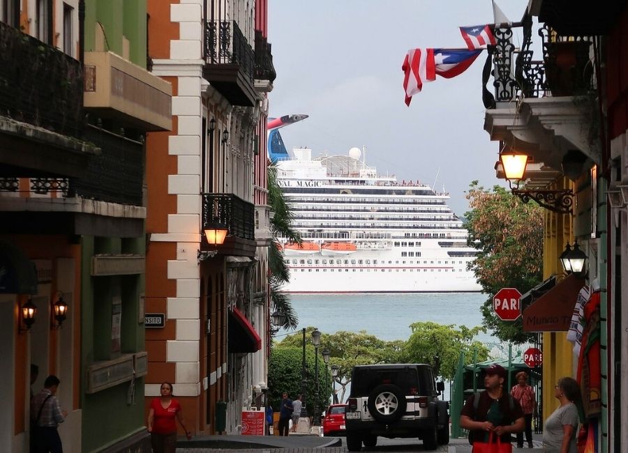 View of a cruise ship in the distance seen from the colourful streets of Old San Juan, Puerto Rico, with people walking nearby