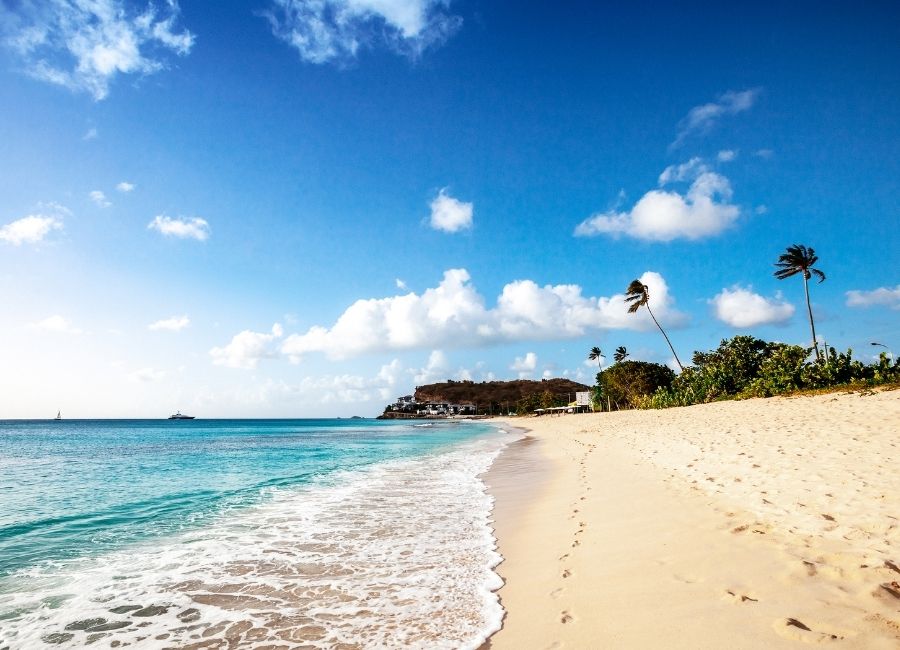 Side view of Darkwood Beach in Antigua and Barbuda, with turquoise water, gentle waves, and a bright blue sky dotted with clouds