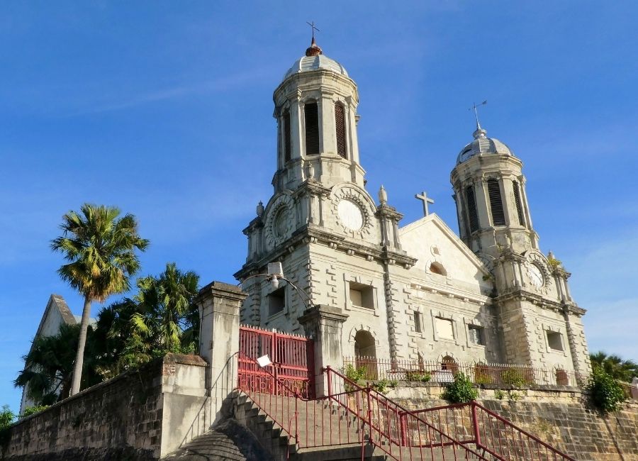 The exterior of St. John's Cathedral in Antigua and Barbuda, featuring twin towers, stone architecture, and a staircase leading to the entrance