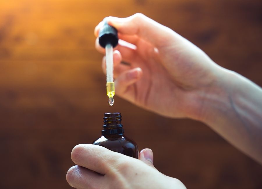 Hand holding a dropper bottle dispensing cannabis oil into an open tincture bottle