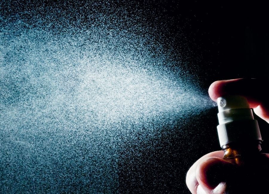 Spray being released from a spray bottle against a dark background