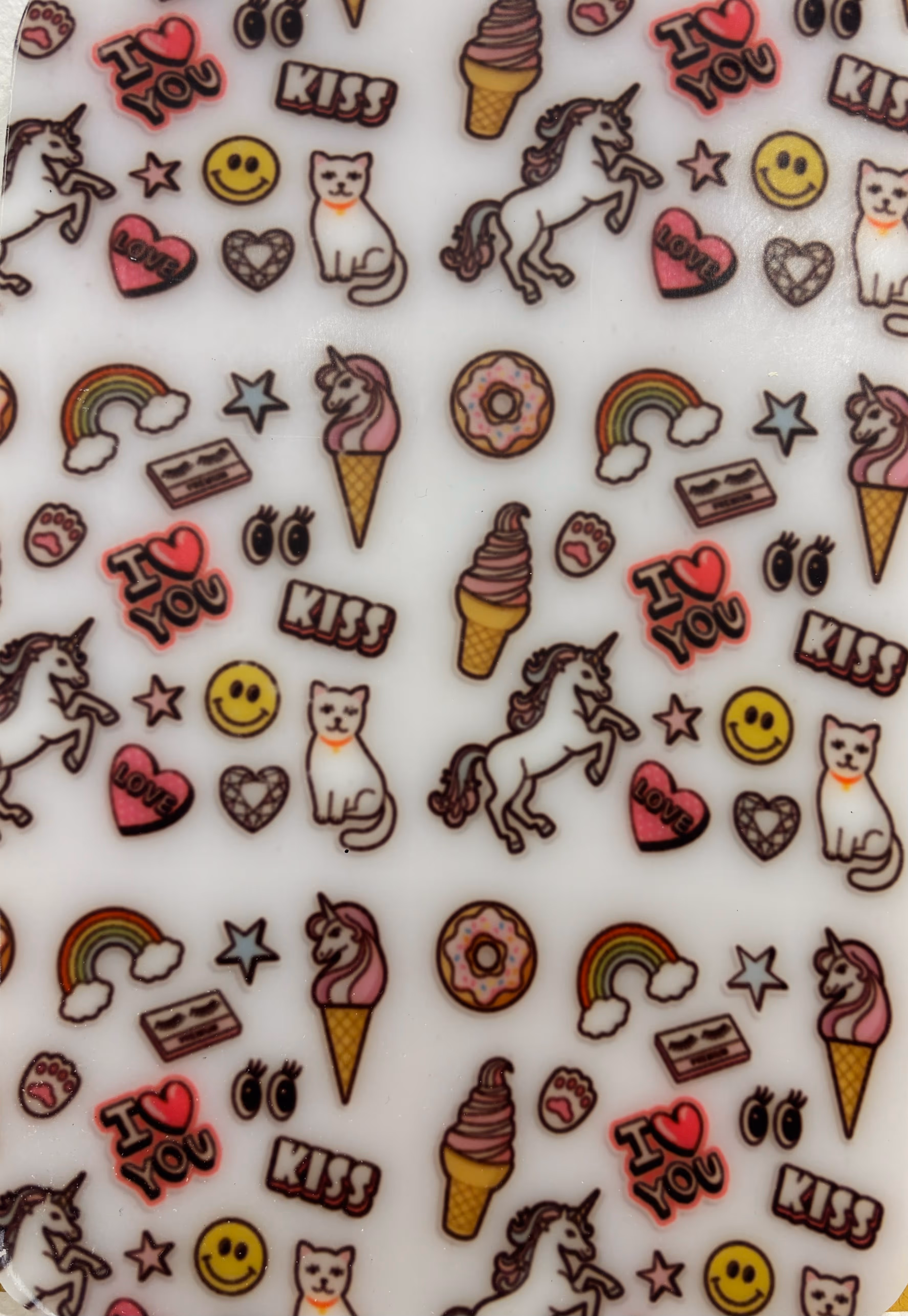 Motifs répétitifs colorés sur fond blanc incluant licornes, chat, glace, arc-en-ciel, donuts, smiley, cœur avec le mot love, mots I love you et kiss, étoiles, pattes et yeux.