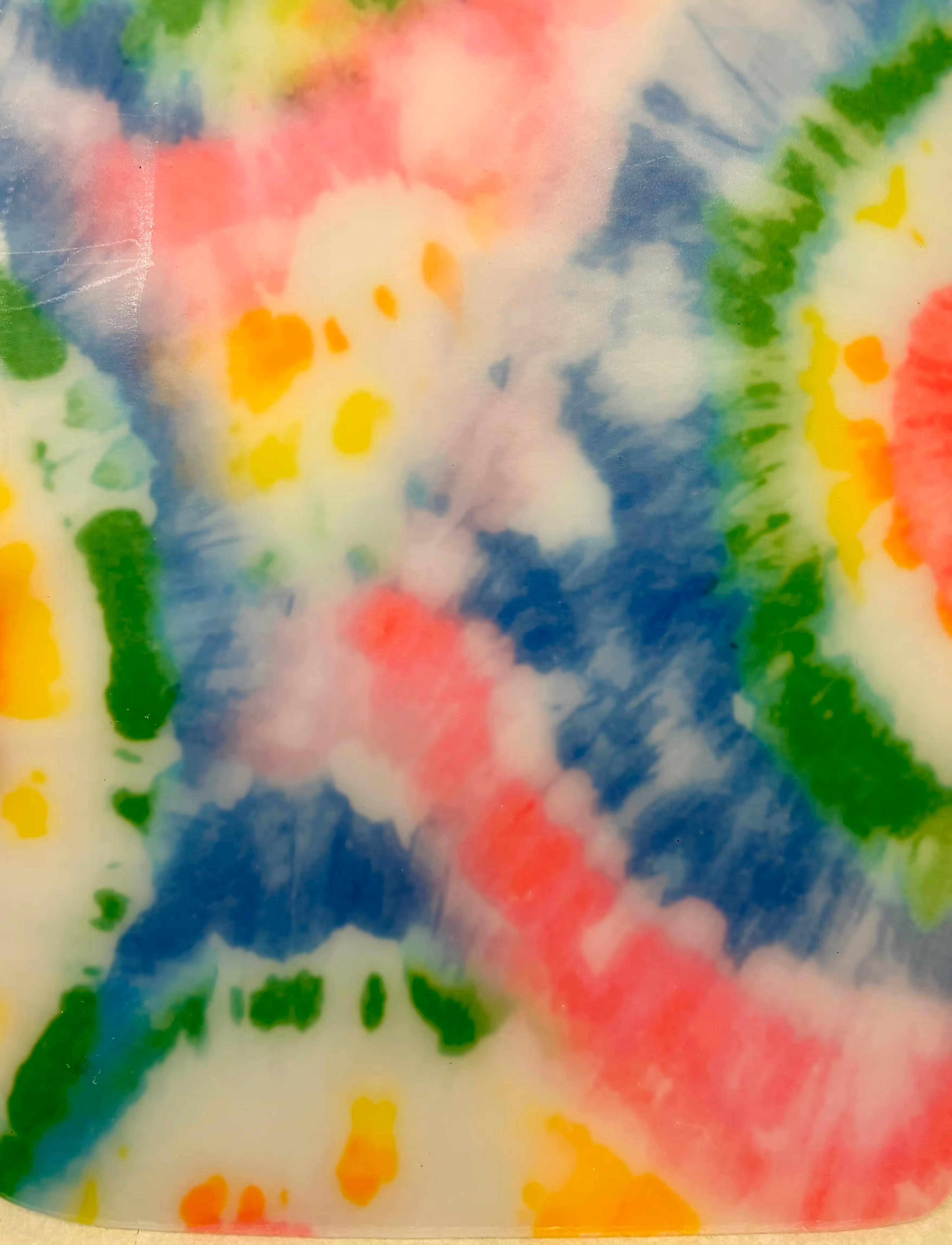 Motif coloré de style tie-dye avec des taches et des cercles flous en rouge, vert, jaune, orange et bleu sur fond clair.