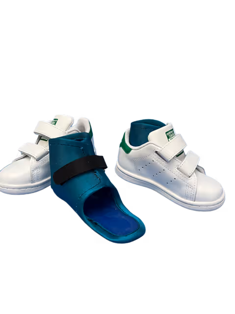 Chaussures blanches Adidas pour bébé avec deux bandes velcro, accompagnées d'un dispositif orthopédique bleu.