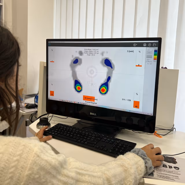 Personne utilisant un ordinateur Dell affichant une analyse de pressions plantaires en couleurs avec des zones chaudes en rouge et jaune.