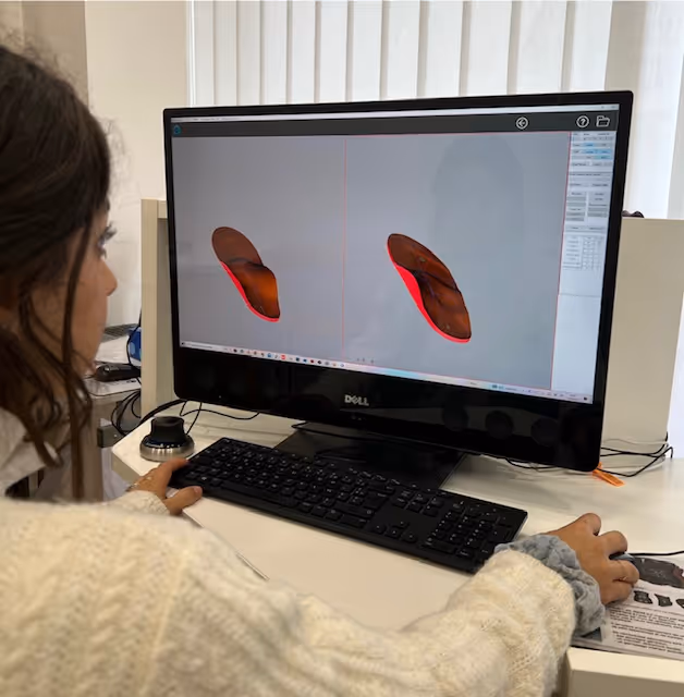 Une personne travaille sur un ordinateur affichant des images 3D d'une semelle de chaussure en rouge et marron.
