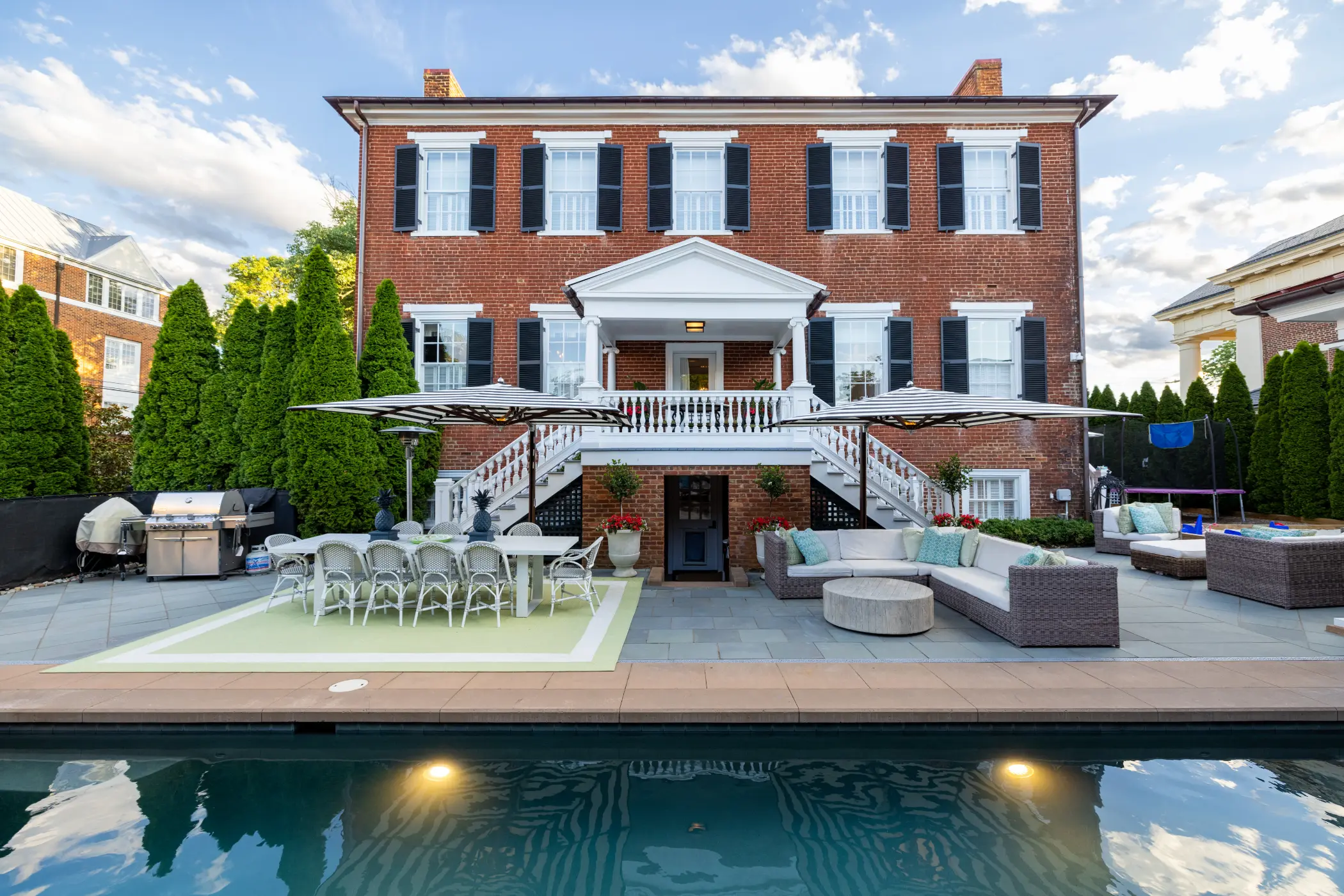 Spacious backyard with a swimming pool, patio furniture, and a large brick house in the background.