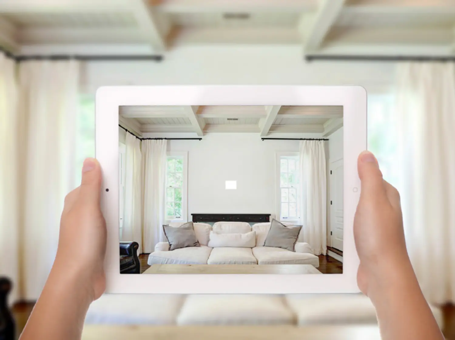 Hands hold a tablet displaying a sofa set in a living room.