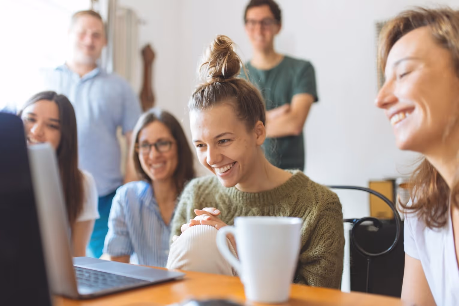 Group of young people smile while sitting around a laptop