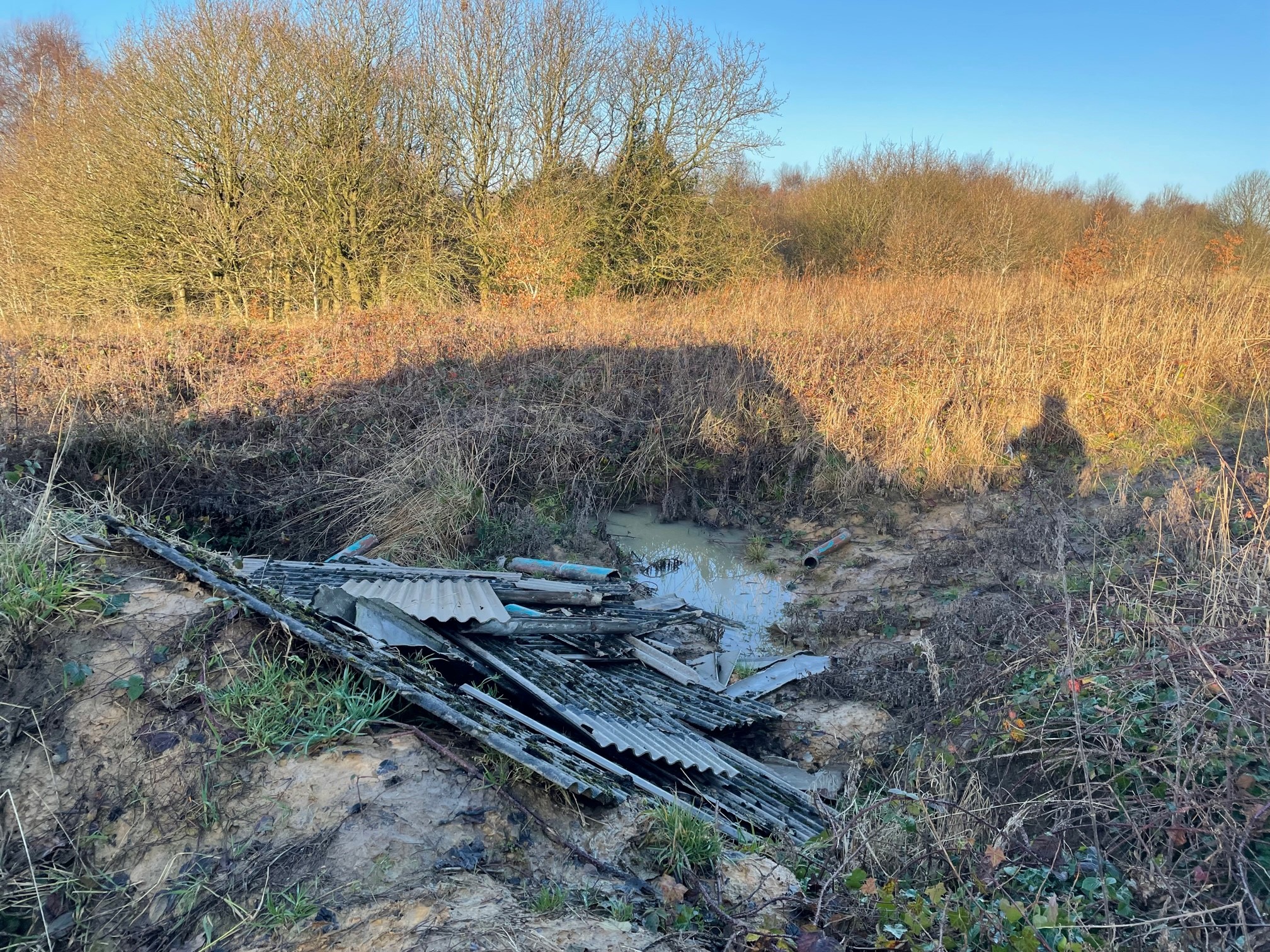 Fly-tipped asbestos cement sheets dumped in a ditch before removal by AIB Solutions