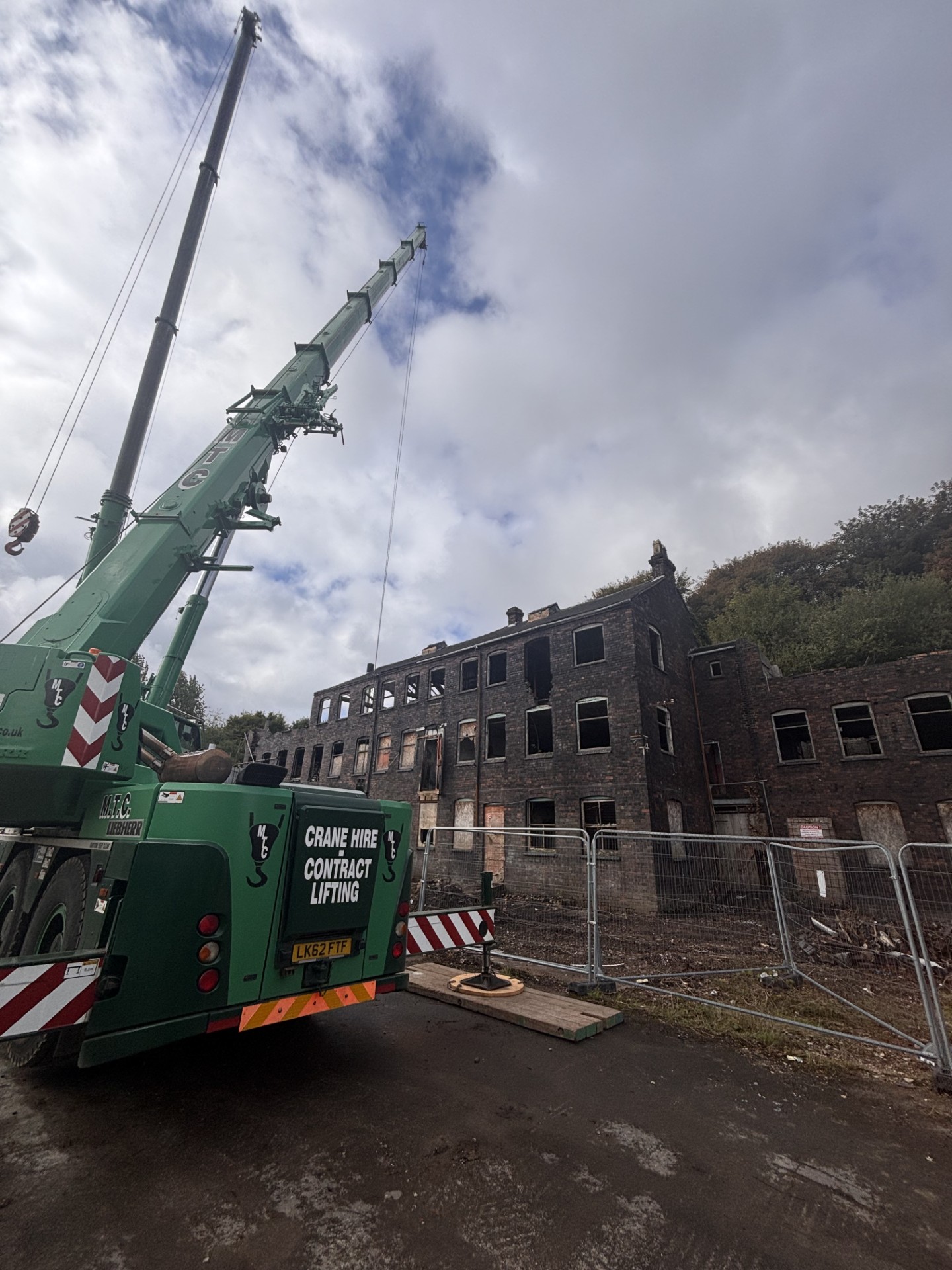 Crane set up on outrigger spreader pads alongside the fire-gutted elevation at Falcon Works