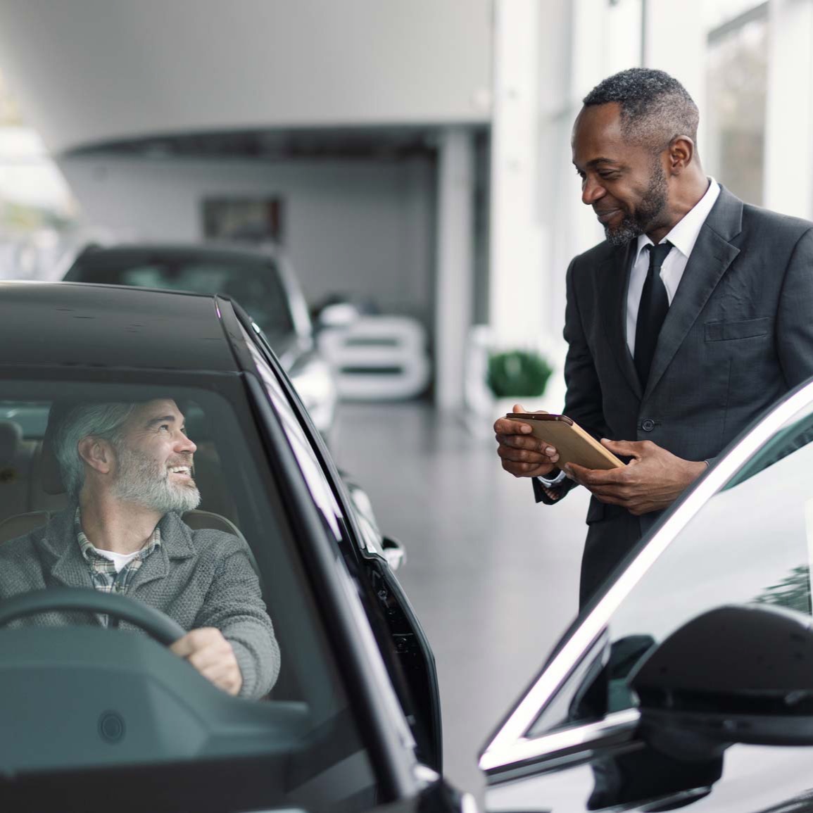 A dealer talks with a customer inside a vehicle during a trade-in appraisal.