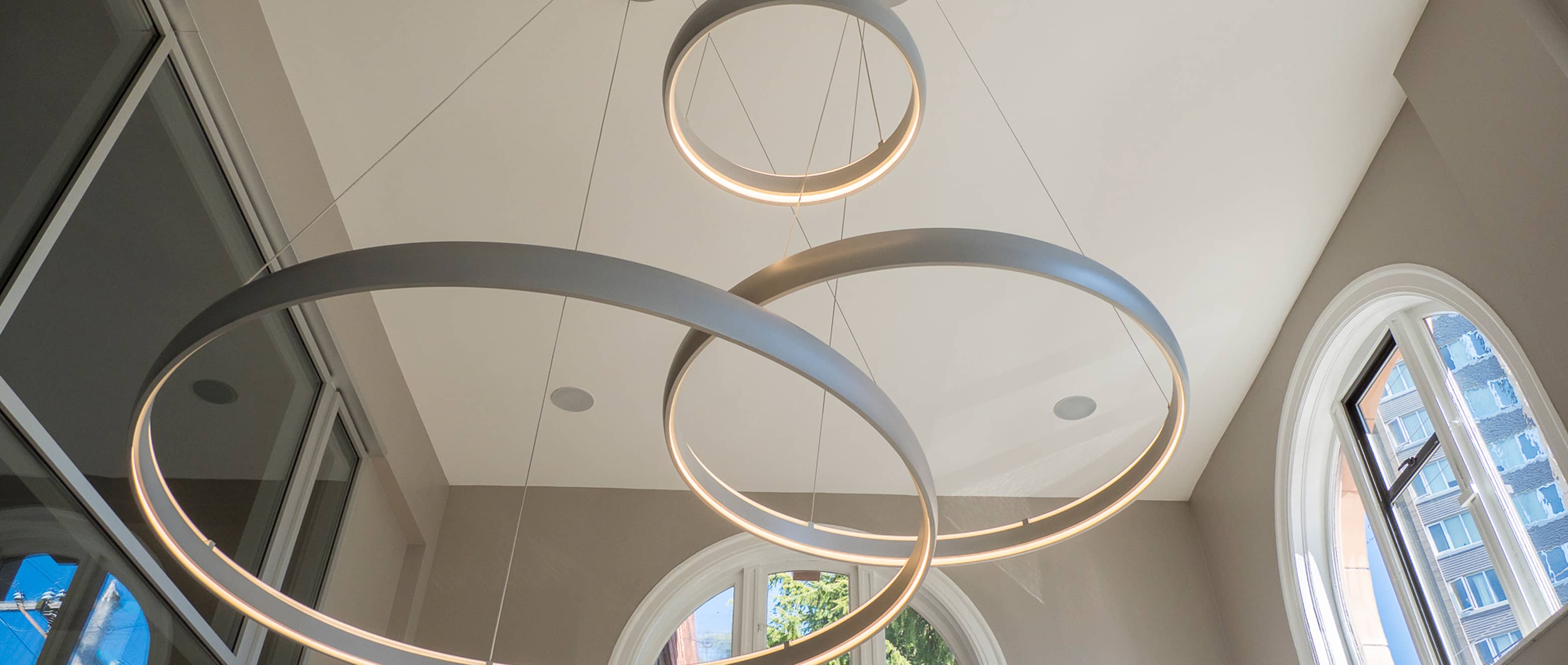 Close-up of modern circular pendant lighting fixtures in a vaulted ceiling space, showcasing architectural integration and precision lighting design. An example of Outlook Project Management’s full-service design-build expertise in Victoria, BC.