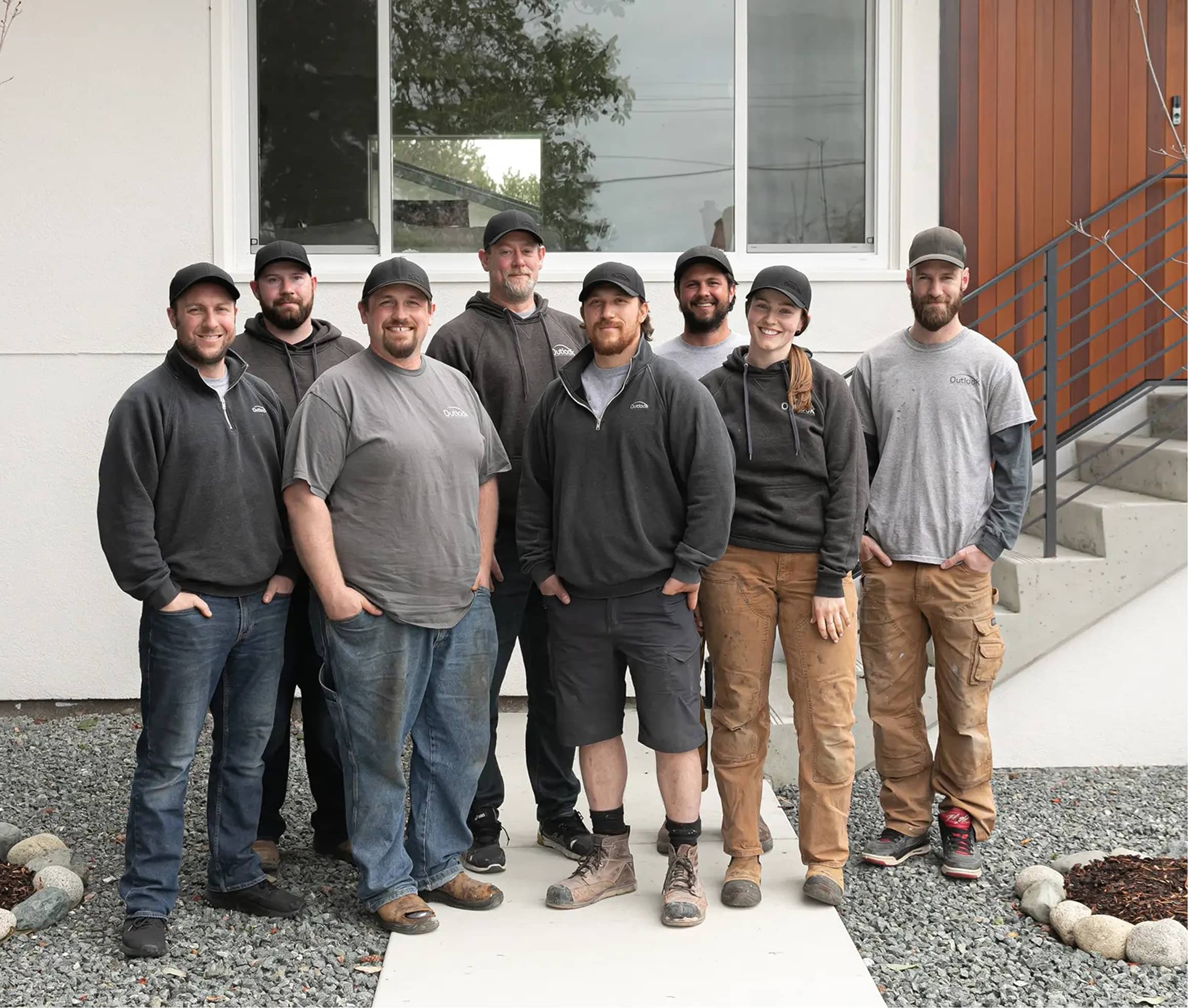 Outlook Project Management crew standing outside a completed residential project, representing the diverse and skilled team featured on the Our Team profile page. The image reflects the company's approachable, hands-on culture and commitment to craftsmanship in Victoria, BC.