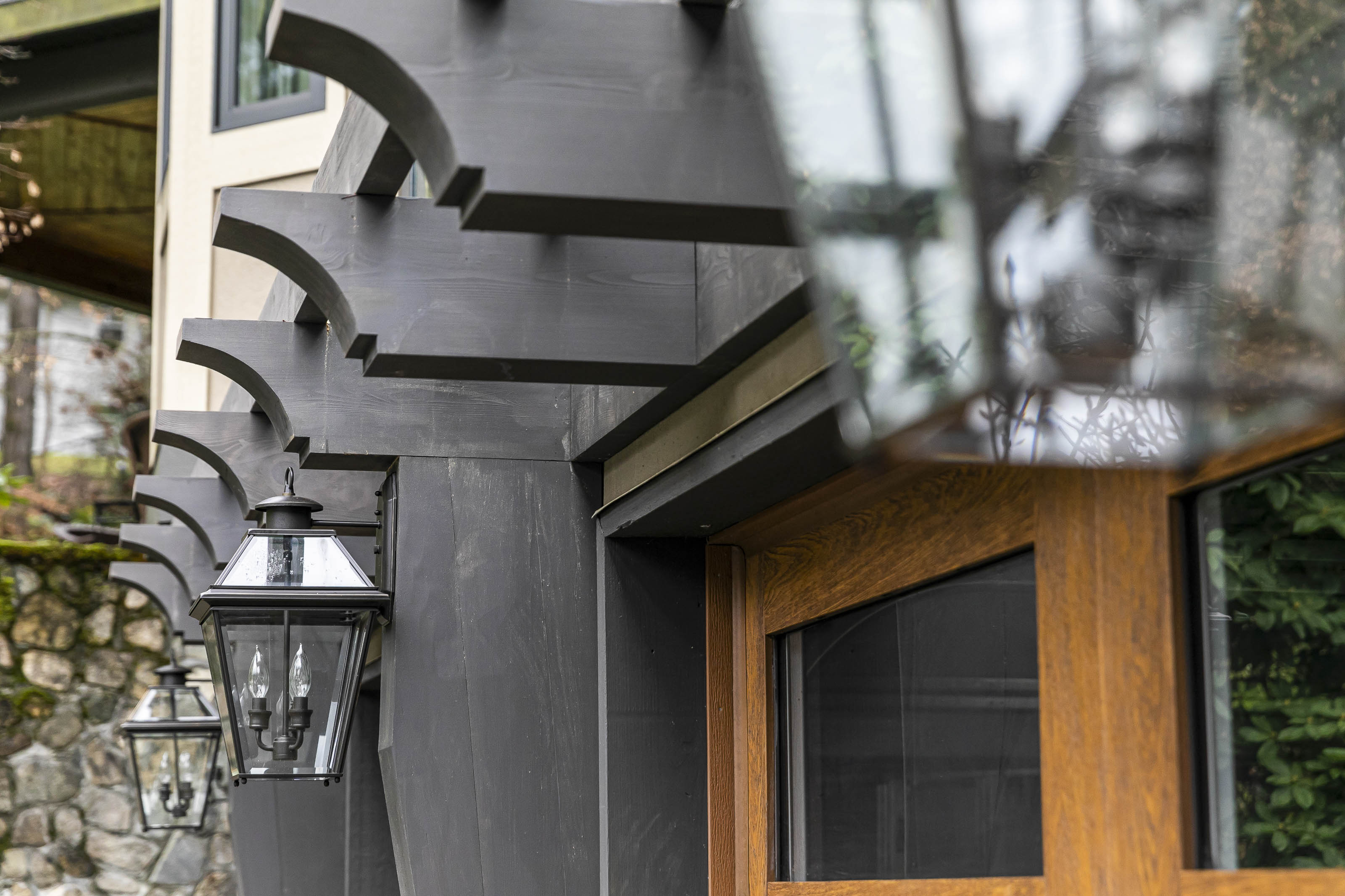 Close-up of custom black timber brackets and classic glass lantern sconces mounted above a wooden garage door at a residential home in Victoria, BC, by Outlook Project Management.