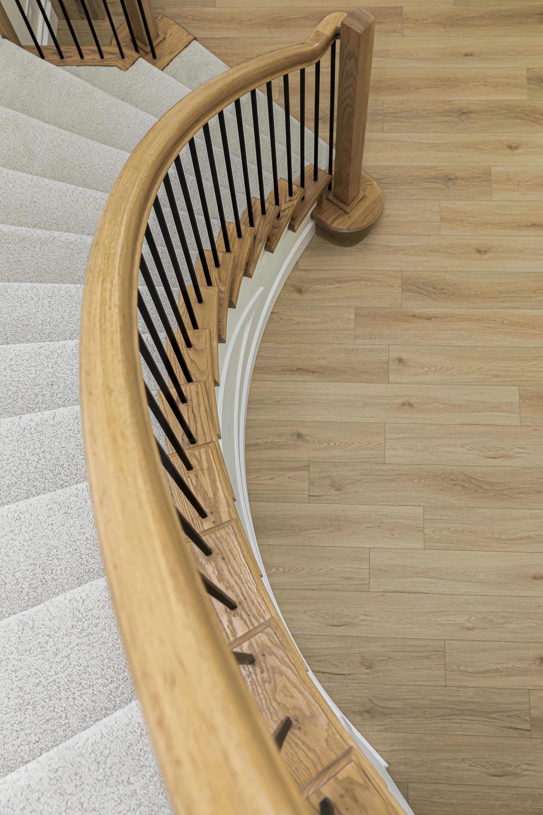 Curved staircase with natural oak handrail and iron balusters from a residential interior project in Victoria, BC.