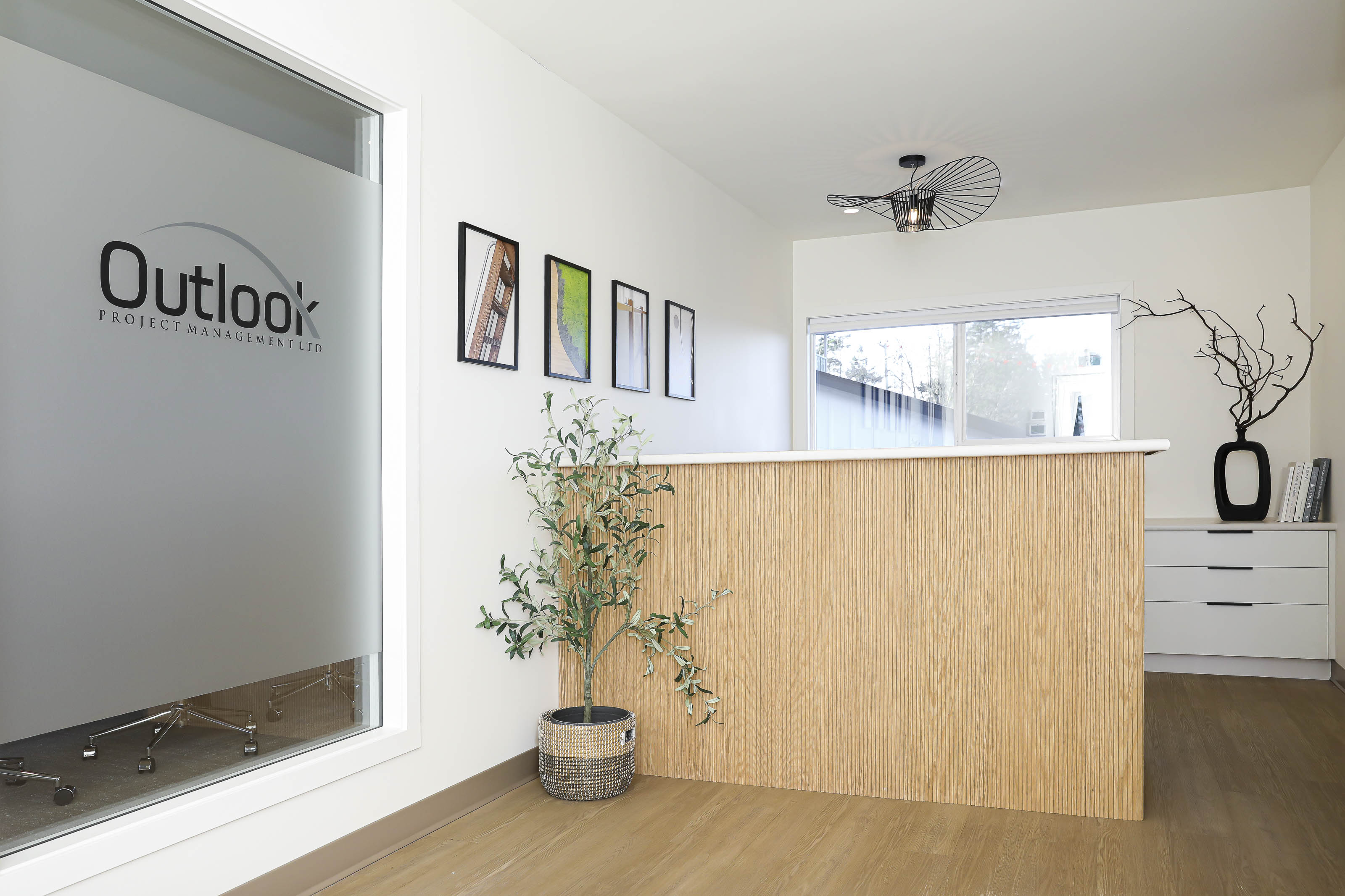 Reception area showcasing a natural wood-fronted desk, large office window, and potted greenery, part of Outlook Project Management’s commercial space in Victoria.