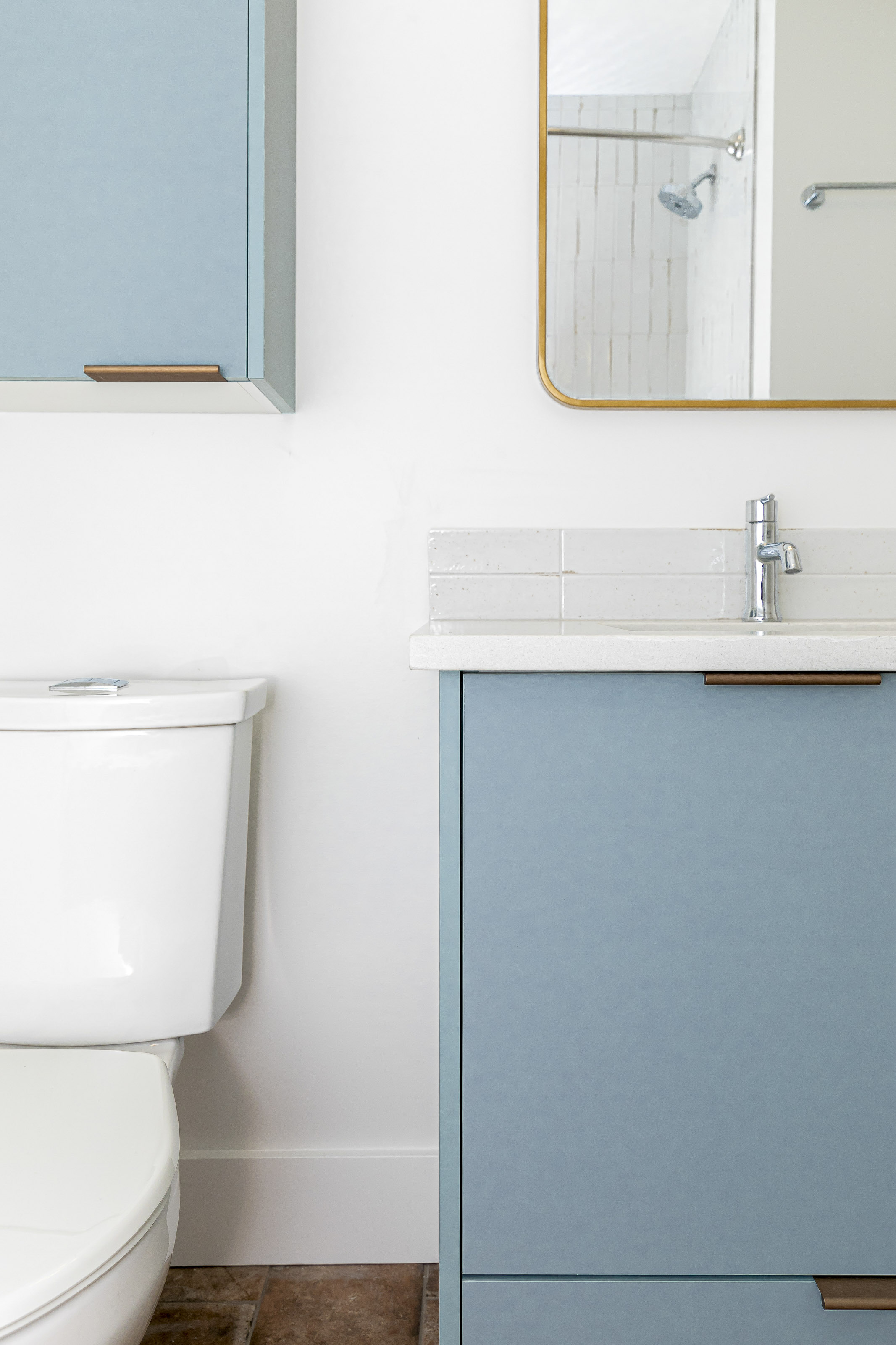 Minimalist bathroom vanity in soft blue with a white countertop and wall-mounted cabinet, alongside a white toilet and gold-edged mirror.