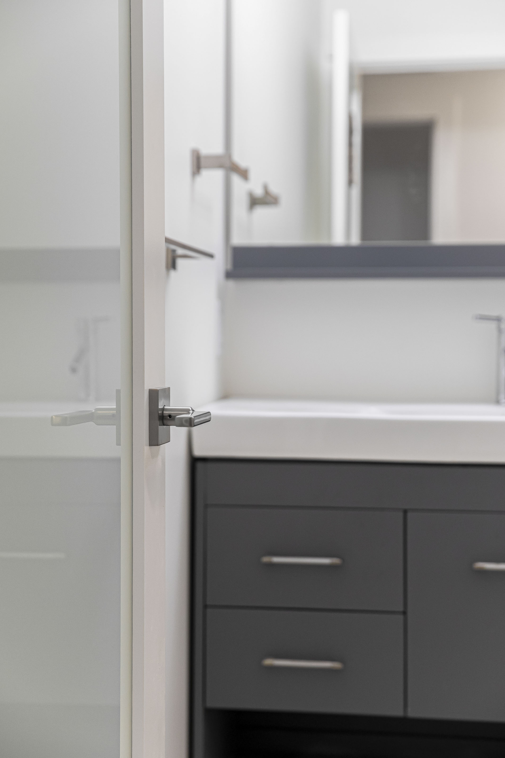 Contemporary bathroom with a matte black vanity, brushed metal hardware, and a frosted glass door in the foreground.