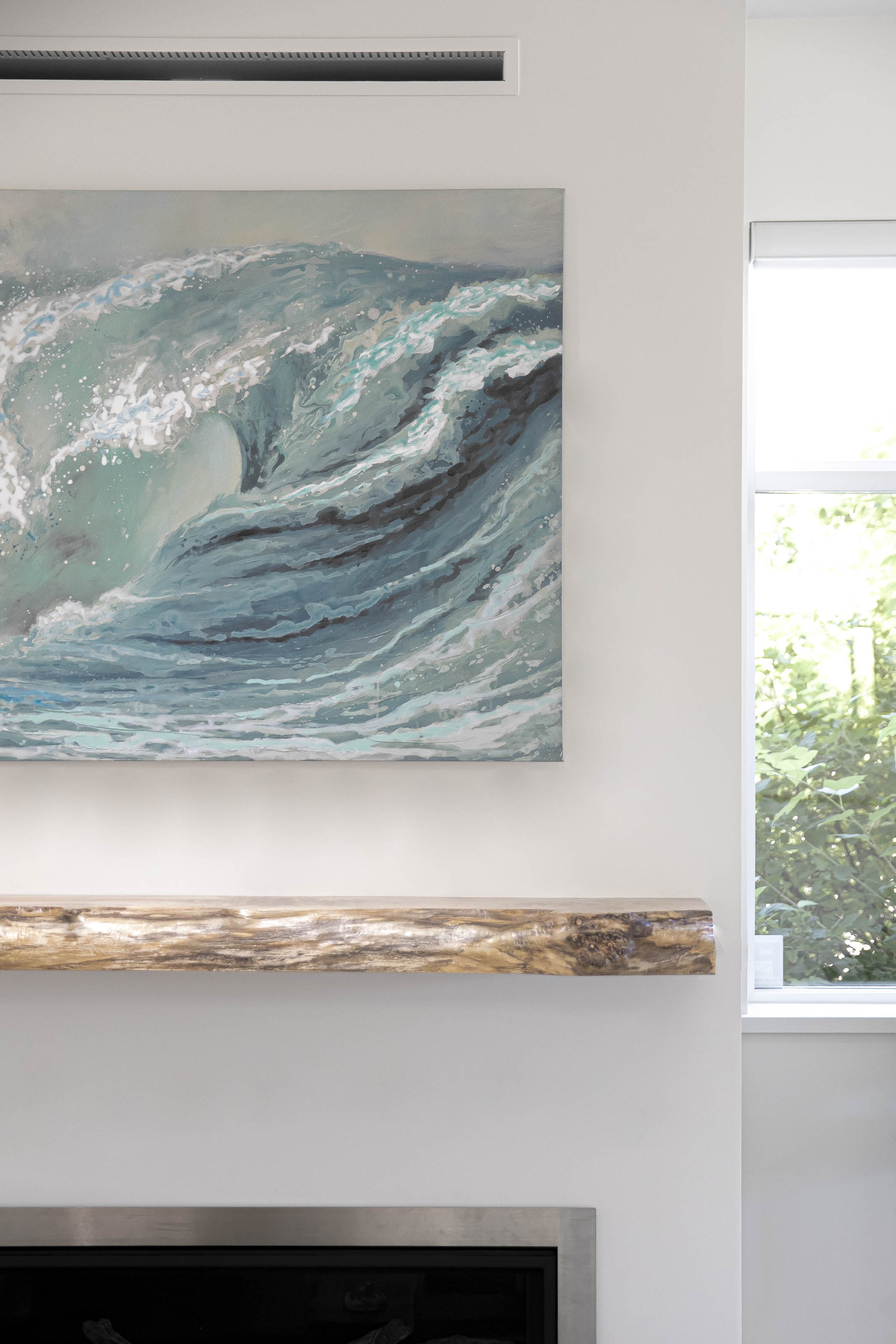 Coastal-inspired painting of an ocean wave above a rustic live-edge wooden mantel and modern fireplace insert.