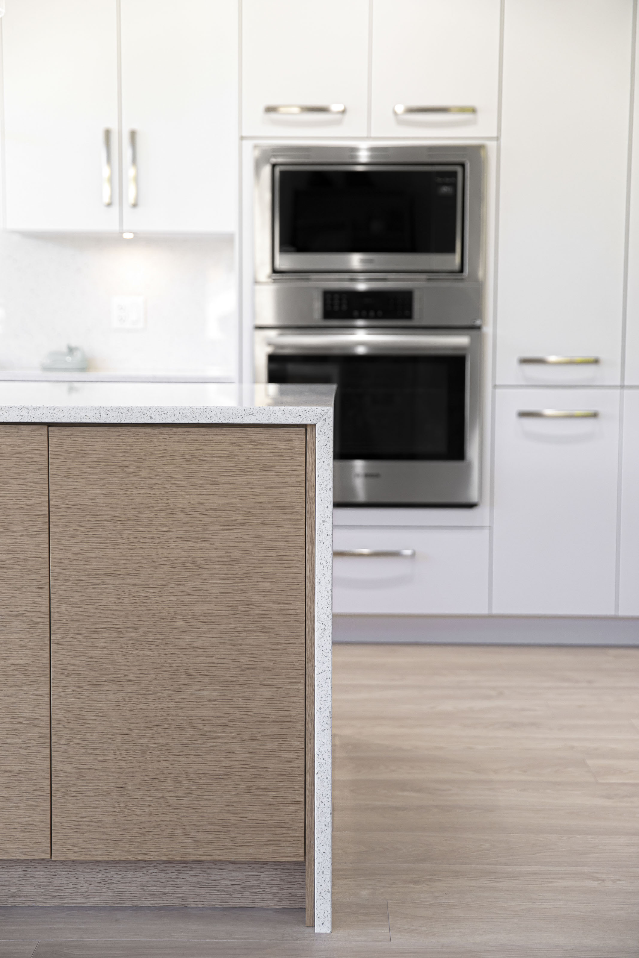 Modern kitchen renovation featuring white upper cabinets, natural wood lower cabinets, stainless steel appliances, and pendant lighting above a large quartz island.