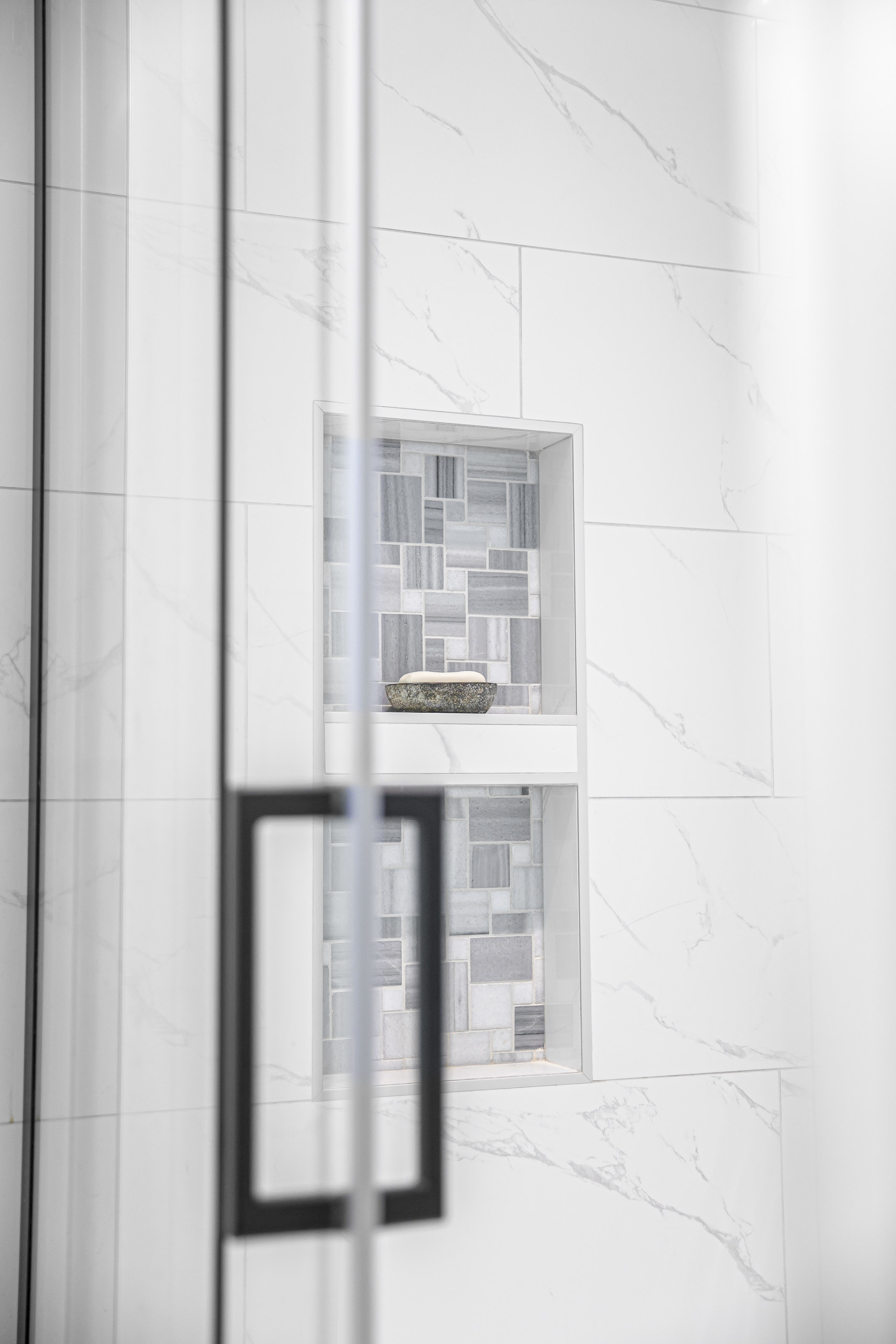 Detail view of a tiled shower niche with geometric grey mosaic tile in a white marble-look surround.