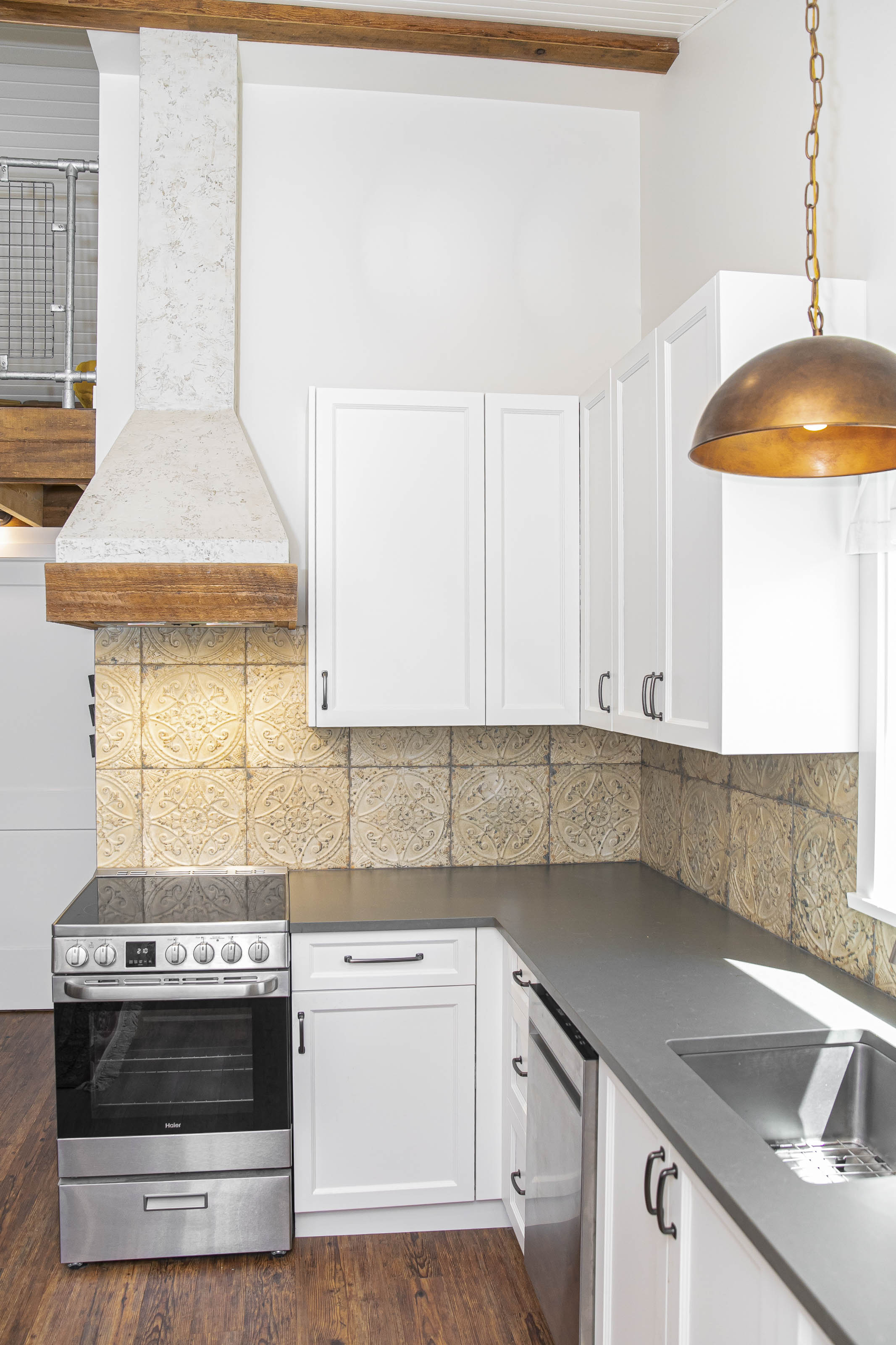 Corner view of a compact kitchen featuring white shaker cabinets, a built-in oven, and rustic tile backsplash in a modern carriage house